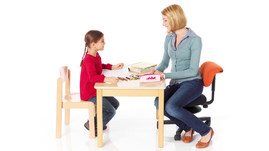 Erzieherin auf einem  Erzieherstuhl am Tisch mit Kind